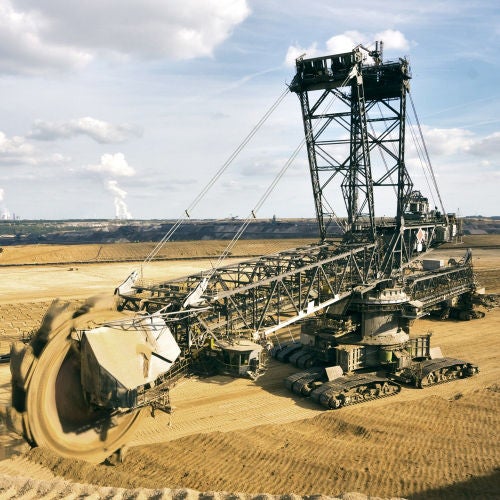 Giant bucket wheel excavator taking away the layers of ground before digging the brown coal. Largest open pit lignite mine in Europe. Power stations at horizon transform the coal to electricity.